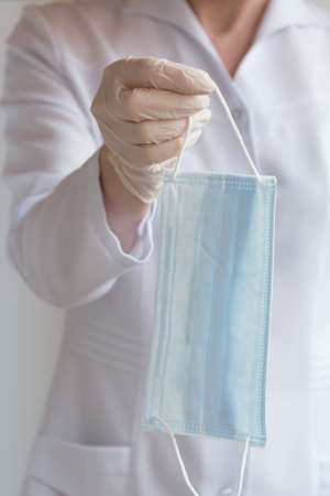 A gloved doctor holds out a medical protective mask. The concept of protection