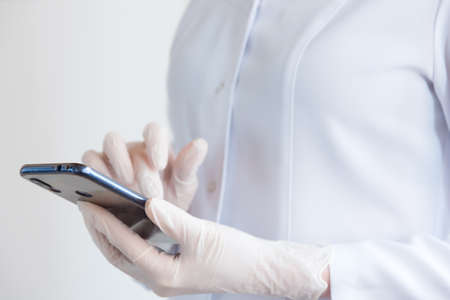 a doctor in latex gloves and a white coat looks at a mobile phone.の写真素材