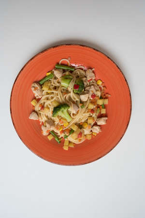 Spaghetti with chicken and vegetables is laid out on a bright orange platter. Close up.の写真素材