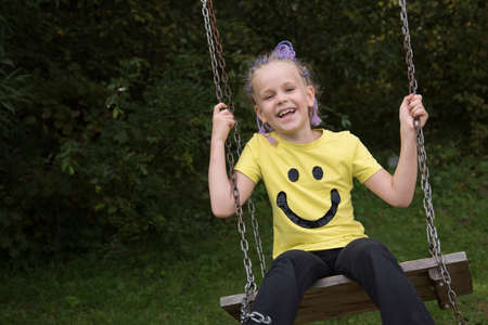 Beautiful little girl on a swing. Happy laughing child. Bright T-shirt with a smile.