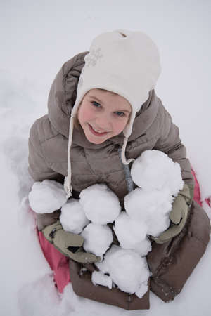 Happy child holding snowballs in hands. A lot of snow, fun and joy. The girl smiles happily. Winter and snowの写真素材
