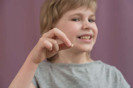 The child holds a lost tooth in his hand. There are traces of caries on the tooth. Removal of a...