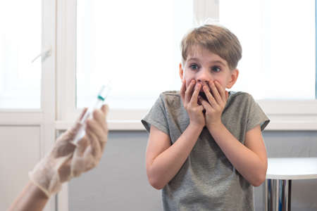 The child looks at the syringe in horror. Fear of injection. Emotions, unwillingness to get vaccinatedの写真素材