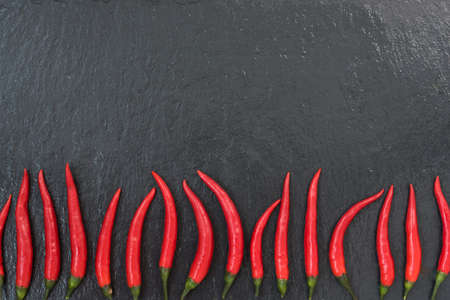 Red chili peppers are laid out on a black slate background. There is room for textの写真素材