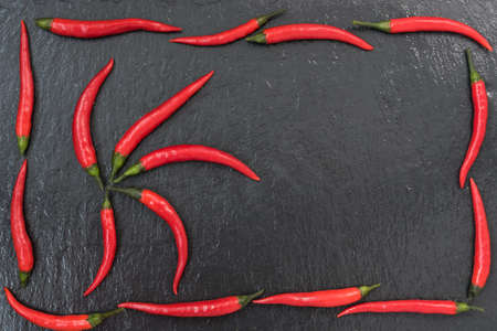 Red chili peppers are laid out on a black slate background. There is room for textの写真素材