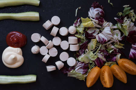 Top view of food. Sausages, fresh herbs and vegetables are laid out on a black slate background. Yellow tomatoes and cucumber. Background, textureの写真素材