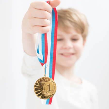 A happy child holds a medal in his hand in front of him. Gold medal. Achievements in sports....