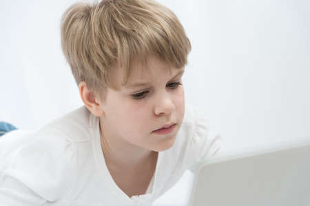 The blond child looks attentively at the computer or laptop screen. Close-up portraitの写真素材
