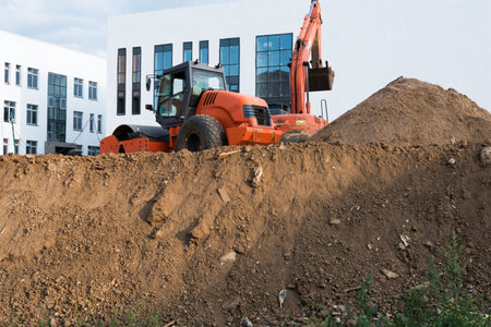 Construction site. Lots of dirt, an excavator and a new white building. Blue sky with clouds
