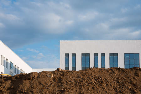 Construction site. Lots of dirt and a new white building. Blue sky with clouds
