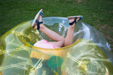 A child in a bumperball. Legs in shorts are visible from an inflatable ball. Fun on the summer lawn.の写真素材