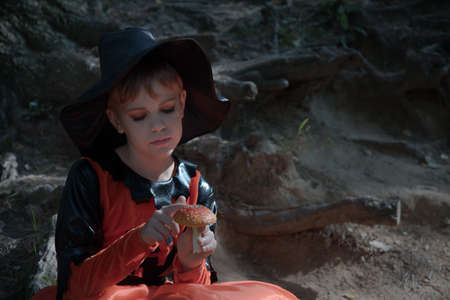 Portrait of a witch. A girl dressed as a witch holds an amanita in her hand. A mushroom for a witchs potion. Beautiful stylish picture in the forestの写真素材