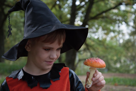Portrait of a witch. A girl dressed as a witch holds an amanita in her hand. A mushroom for a witchs potion. Beautiful stylish picture in the forestの写真素材