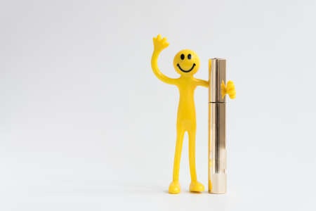 Happy smiling yellow man. The little man holds ink in one hand, the other hand is raised up. The right choice of mascara. Conceptの写真素材