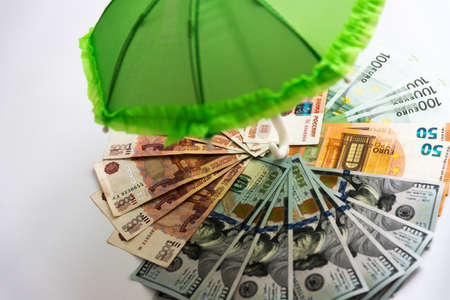 There are 3 different currencies under the open umbrella. Russian ruble, euro, dollar. Tricycle basket. Storing savings in different currencies to reduce risks. Financial protection. Conceptの写真素材