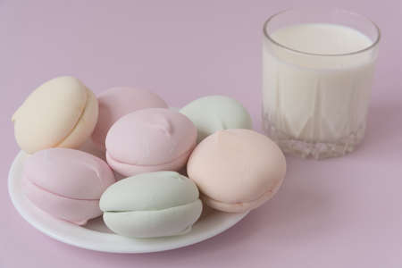 On the plate is marshmella of different colors. Nearby is a glass of milk. Pink background. Cozy...