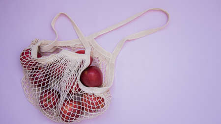 Mesh Shopping Bag. Juicy red apples are in the bag. Delicate pink background. Caring for the Environment. Healthy, organic fruitsの写真素材