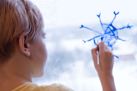 A child draws a Christmas snowflake on the window. A snowflake in the form of a coronavirus. The concept of Christmas and quarantine. The concept of the New Year during the pandemic. Stay home.の写真素材