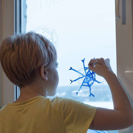 A child draws a Christmas snowflake on the window. A snowflake in the form of a coronavirus. The concept of Christmas and quarantine. The concept of the New Year during the pandemic. Stay home.の写真素材