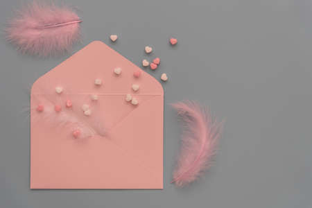 Delicate shades to create a valentine. Pastel colors, top view. Pink envelope, feathers and hearts on a gray background. Theres room for text. Invitation to a wedding, birthday or valentine.の写真素材
