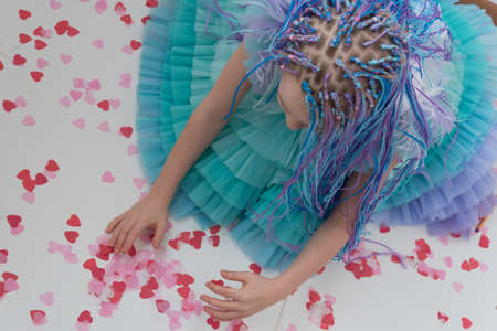 A teenage girl in a beautiful evening puffy dress collects confetti from hearts. Concept, Valentines...