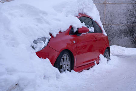 Red car in the parking space. The car is covered in snow. Huge snowdrift on the carの写真素材