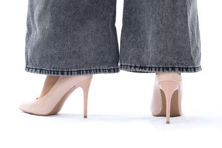 Womens legs in elegant patent leather high-heeled beige shoes. Gray wide leg jeans. View from