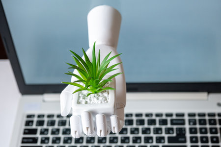 Directly from the monitor, the robot hand holds out a flower to the buyer. The concept of fast delivery of goods. The concept of buying plants via the Internetの写真素材