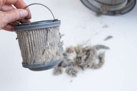 A womans hand holds a dirty vacuum cleaner filter. The miniature vacuum cleaner has collected a lot...