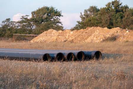 Pipes for laying water pipes lie on the lawn. Sunset, the rays of the sun illuminate the construction siteの写真素材