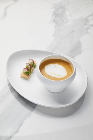King prawn bisque served with crusty bread, Creamy prawn soup in a cup on white marble background