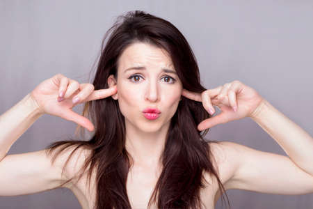 Beautiful woman covering her ears making a silly faceの写真素材
