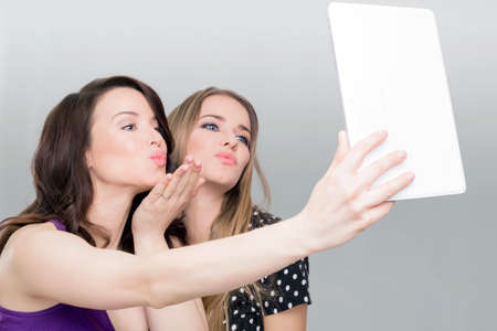 Two women taking a selfie on a white tabletの写真素材