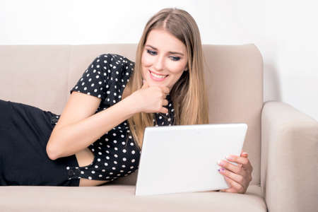 Woman on a sofa, looking at a white tabletの写真素材