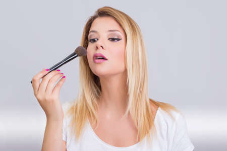 Blonde girl applying makeup with a brushの写真素材