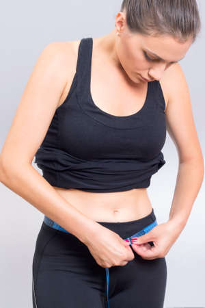 Brunette fit woman measuring her waist with meter