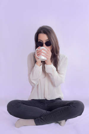 Hipster woman drinking tea on a pastel lavender backgroundの写真素材