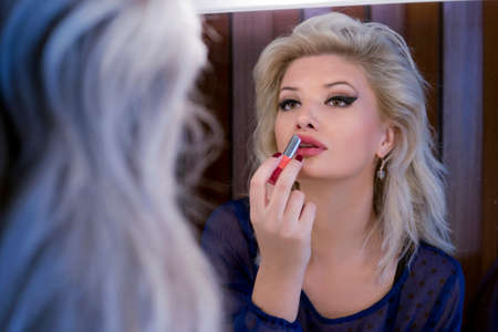 Gorgeous blonde woman putting on lipstick in a mirrorの写真素材