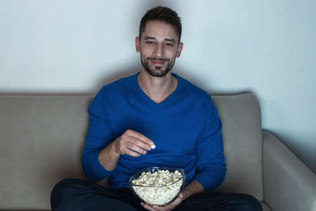 Man eating popcorn, watching televisionの写真素材