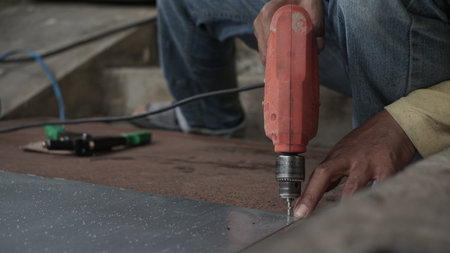 Worker using a drill to cut a metal sheet at a construction siteの写真素材