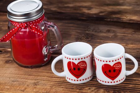 A glass jar of jam and two cups with hearts on a wooden tableの写真素材