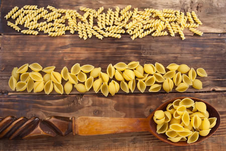 Different kinds of pasta macaroni on a wooden table in a spoonの写真素材