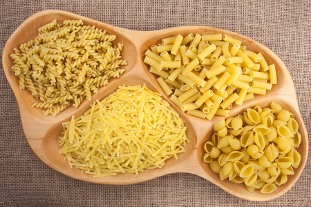 Different kinds of pasta macaroni in a plate on a textureの写真素材