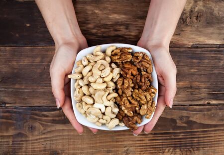 Plate with different kinds of nuts in a plate in the hands on wooden tableの写真素材