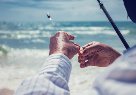 Close up the fisherman puts the worm on a fishing hook in the beach sunny dayの写真素材