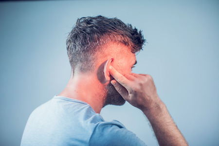 male having ear pain touching his painful head isolated on gray backgroundの写真素材