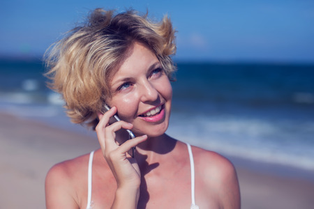 Young happy woman talking on mobile phone on a beach with sea backgroundの写真素材
