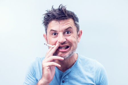Handsome young man with brown hair wearing shirt isolated on grey background. Smoking cigarette.の写真素材
