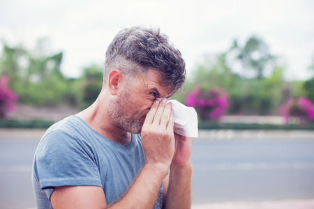 Man sneezing in a tissue outdoors. Pollen allergy, Springtime.の写真素材