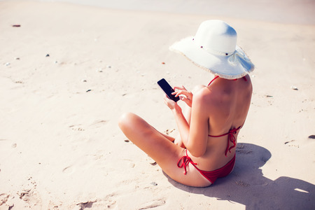 Young woman in hat with mobile phone at the beachの写真素材